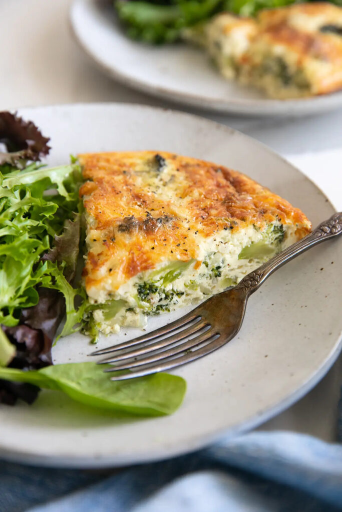 small serving plate with a single slice of crustless quiche and a side of mixed green lettuce