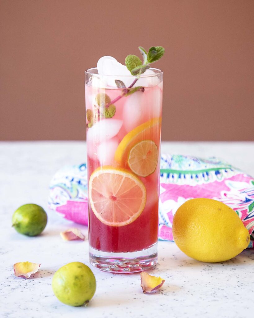 a glass of hibiscus lemonade with ice and sliced lemons