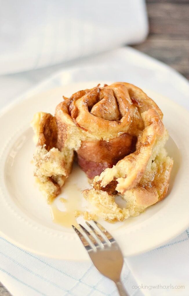a maple bacon cinnamon roll in a white plate with fork