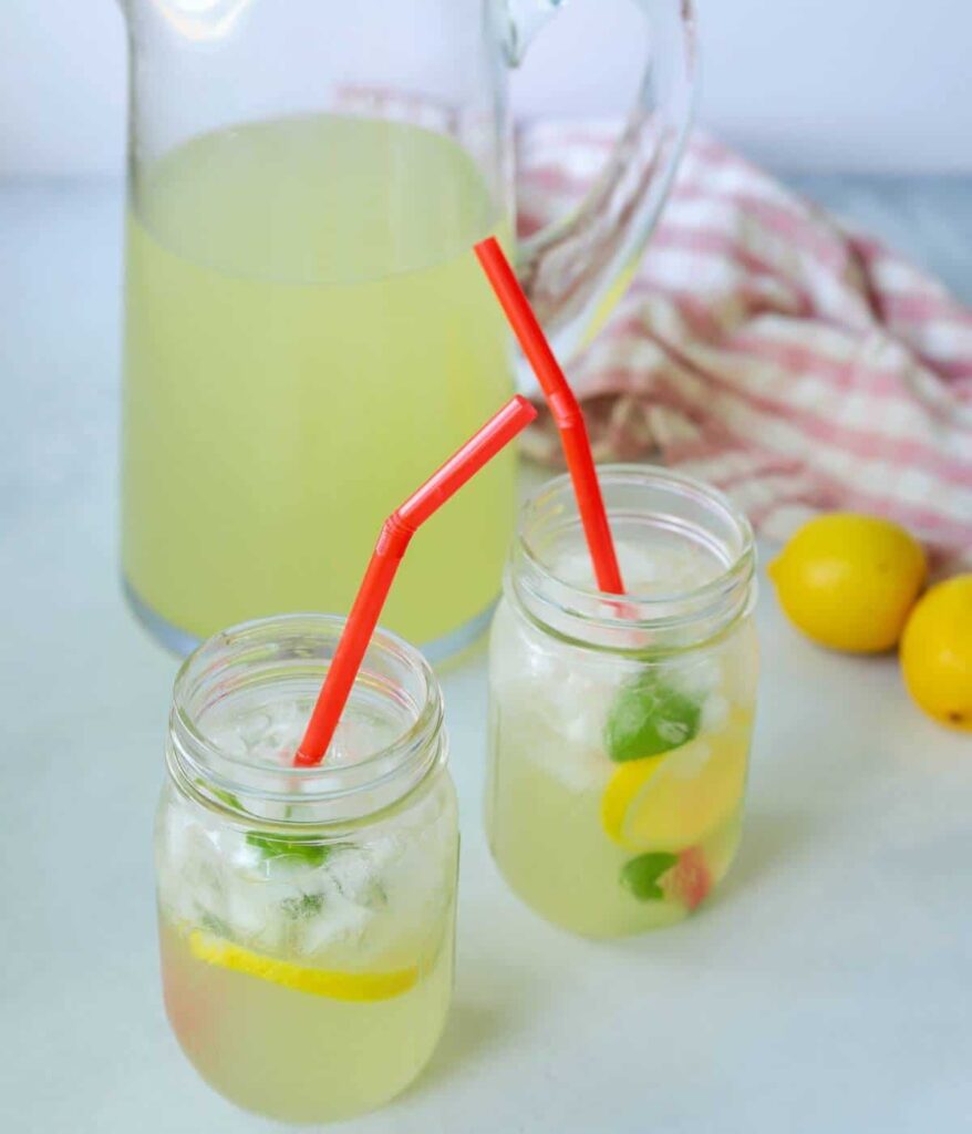 Two mason jars full of lemonade with a pitcher next to them