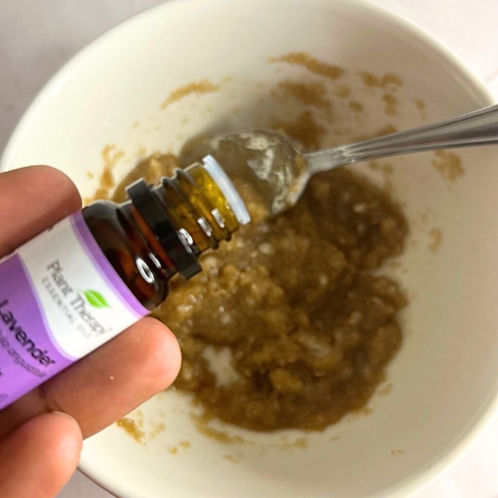 hand holding lavender essential oil to place in bowl with sugar