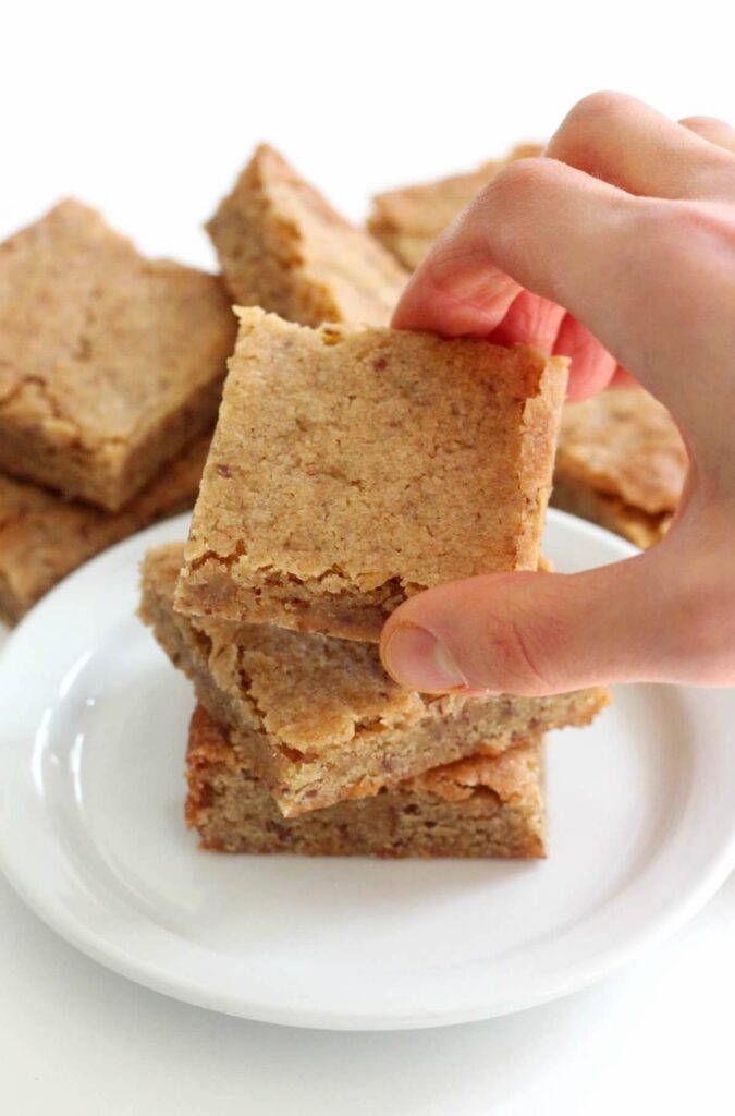 hand getting a piece of gluten-free maple blondie from a white plate