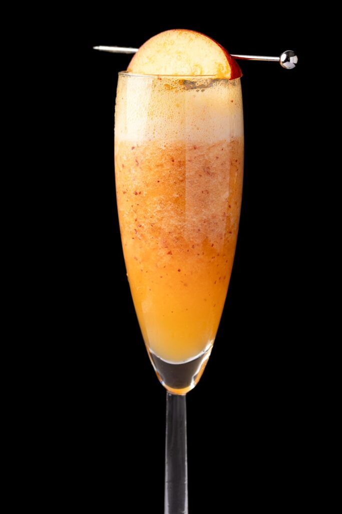 A non-alcoholic peach bellini garnish with a slice of fresh peach, on a black background