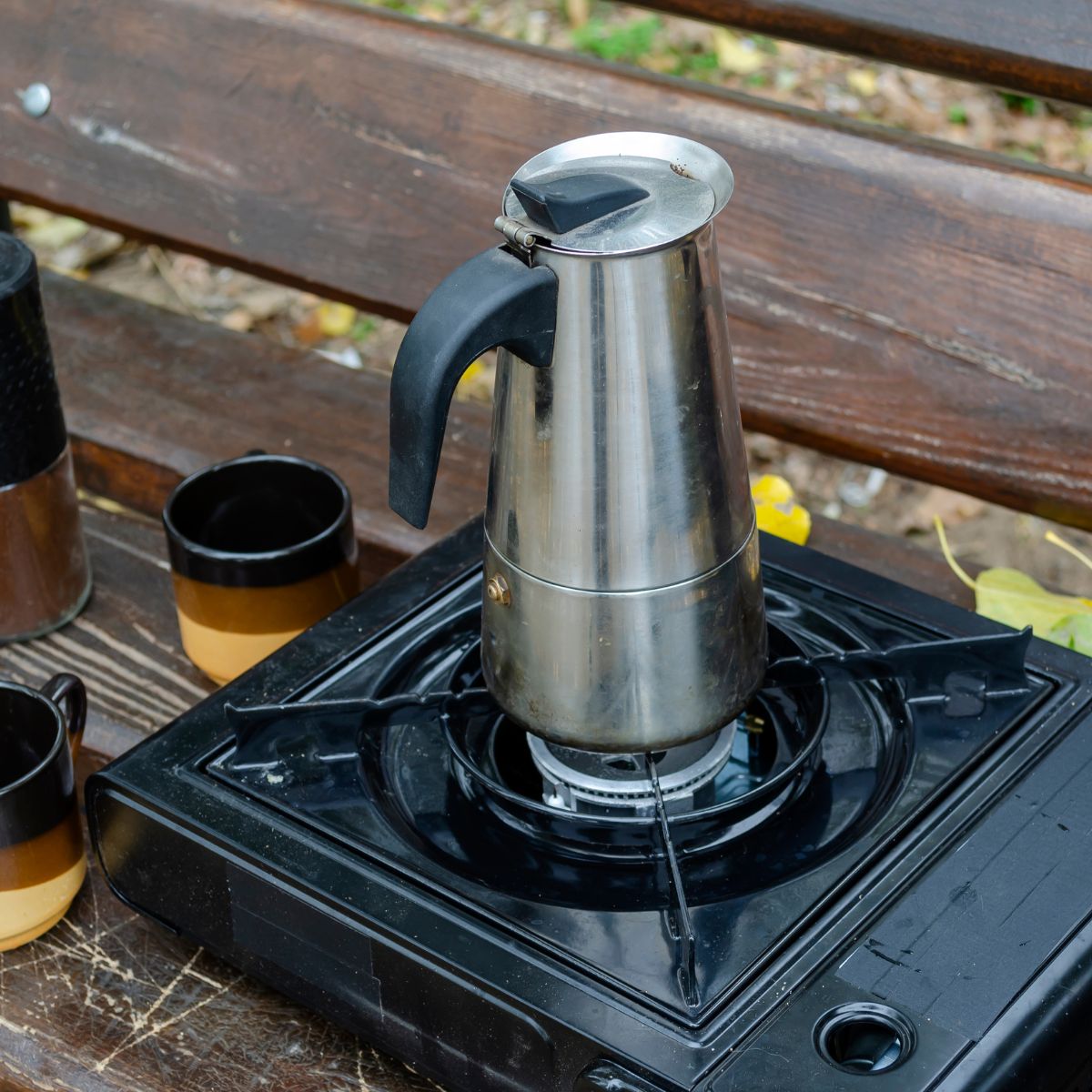 a coffee pot sitting on top of a portable stove placed on a wooden picnic table