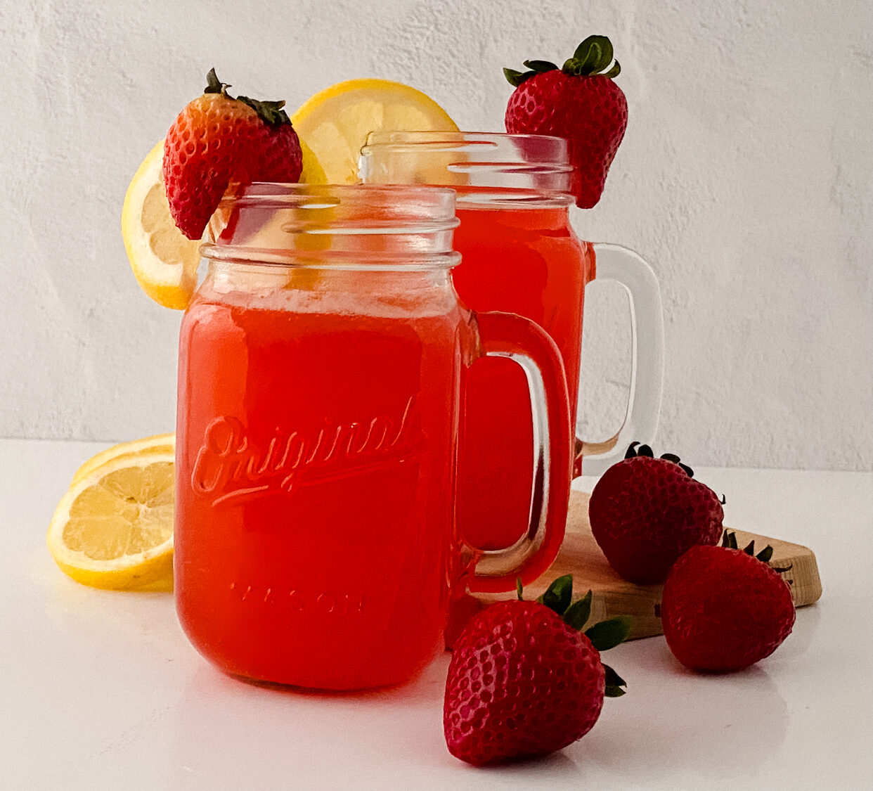two pitcher of strawberry lemonade with sliced fruits at the mouth