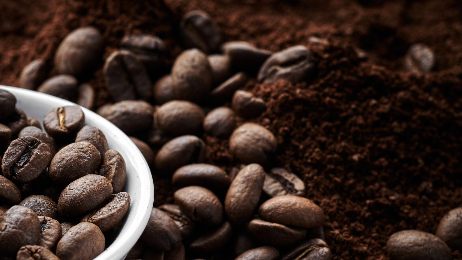 Roasted coffee whole and ground beans in bowl isolated close up on brown grunge background