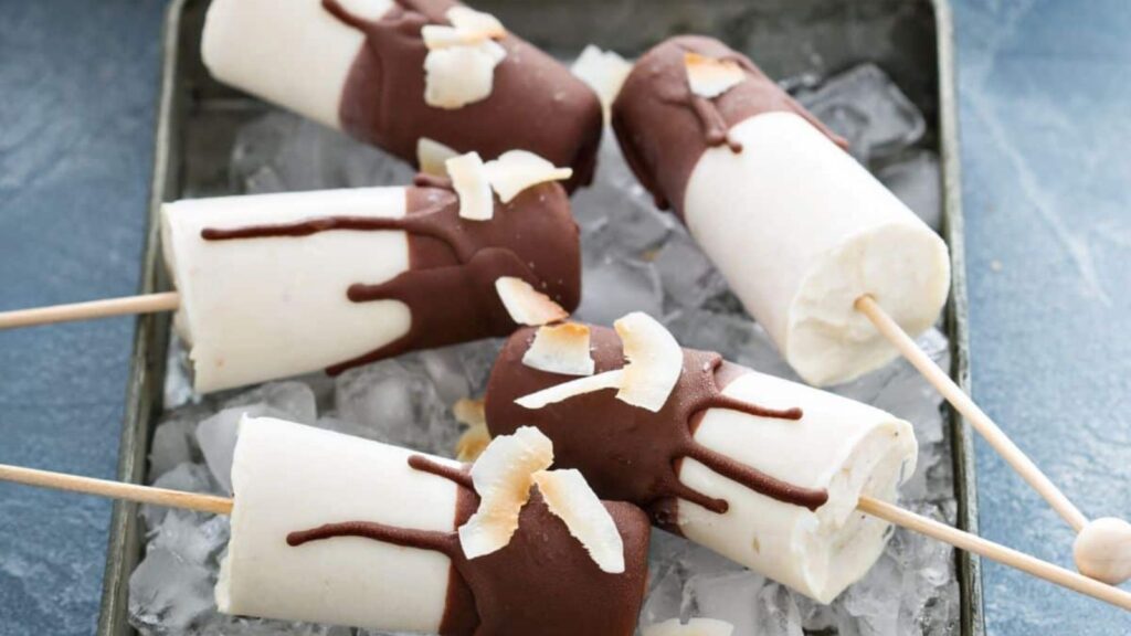 21 Delightful Homemade Popsicle Recipes 2 Banana popsicles covered in chocolate sitting in a pan with ice.
