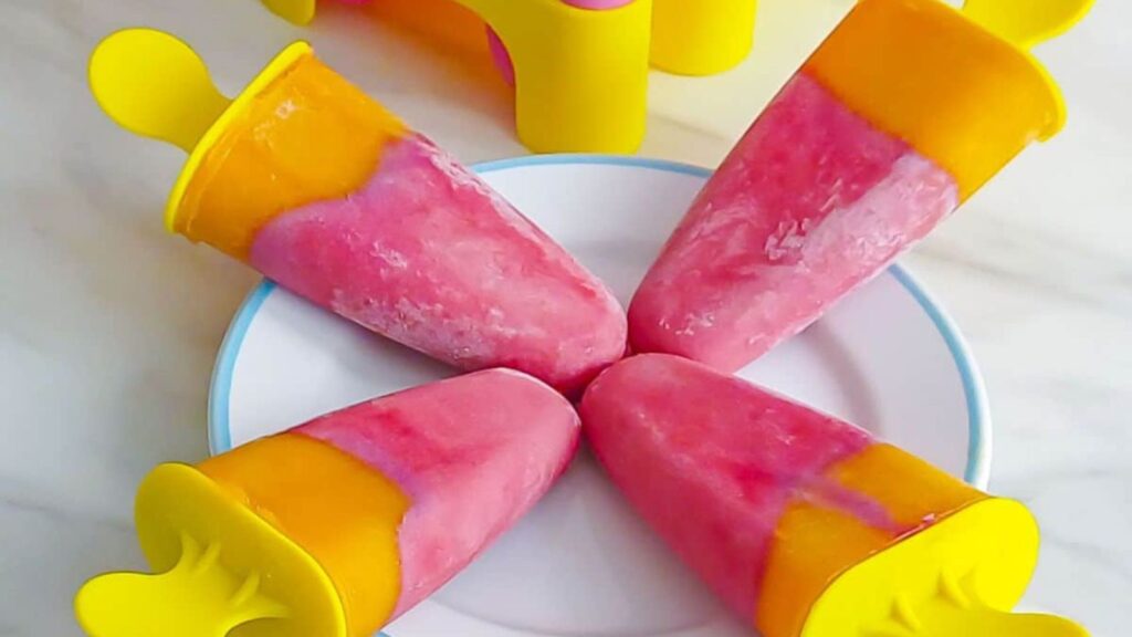 21 Delightful Homemade Popsicle Recipes 15 Four pink and yellow popsicles on a white plate placed on a marble along with popsicle base behind them.