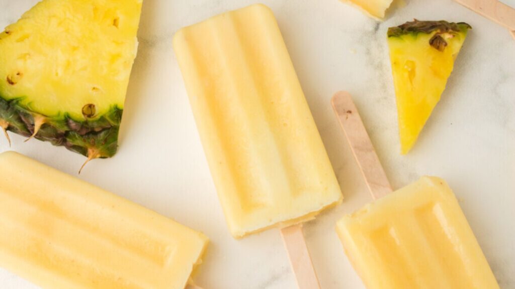 21 Delightful Homemade Popsicle Recipes 19 ice cream dole whip popsicles laid on a countertop with pineapple slices