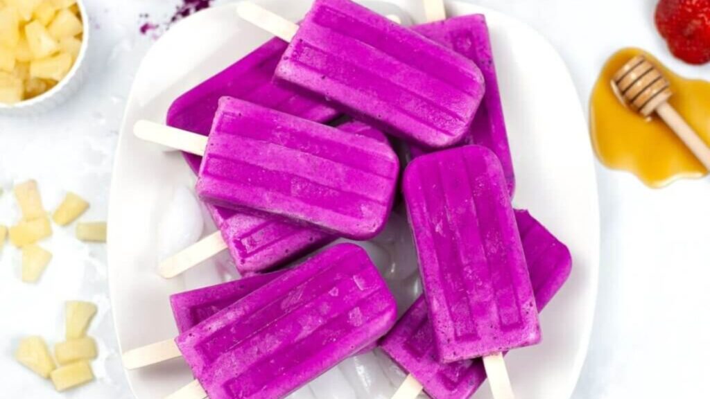 21 Delightful Homemade Popsicle Recipes 18 Dragon Fruit Popsicles piled on a plate surrounded by fruits.