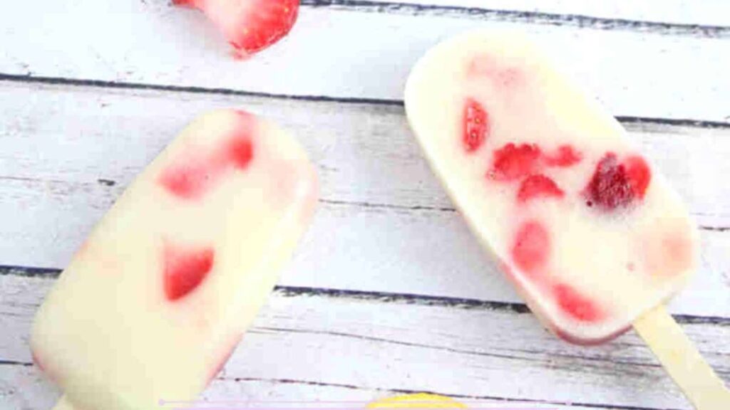 21 Delightful Homemade Popsicle Recipes 4 Strawberry yogurt protein popsicles laying flat with strawberries, a honey stick, and lemons around them.