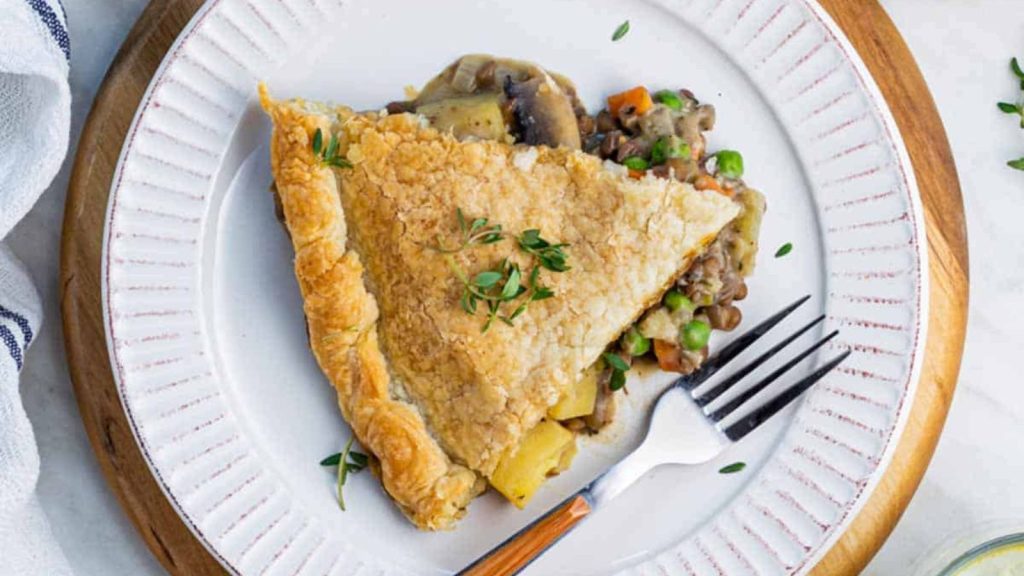 28 Incredibly Tasty Mushroom Recipes With Freshly-Foraged Flavors 12 A piece of lentil pot pie served on a white plate, placed on a round wooden cutting board.