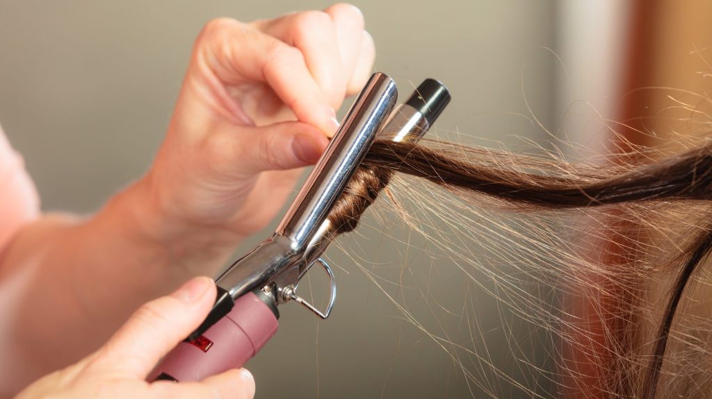 Stylist curling hair for young woman.