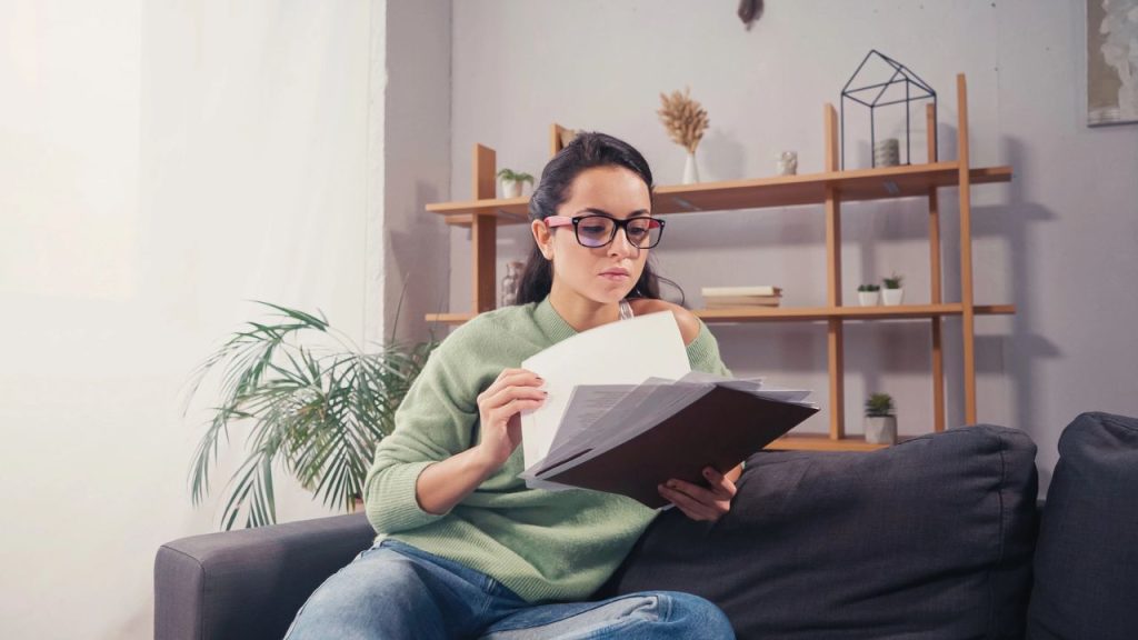 15 Bills You Should Always Pay Early to Avoid Stress and Fees 5 Brunette student in eyeglasses holding papers on couch