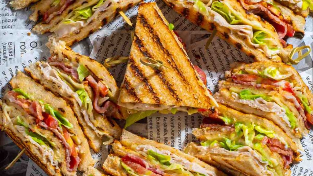 25 Gourmet Sandwiches Perfect for Your Next Lunch Break 7 Club sandwiches on a tray lined with newspaper.