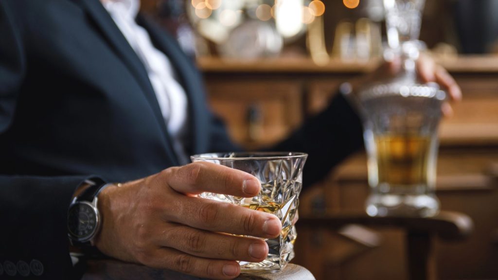 Cheap Items that Will Be Valuable When SHTF 3 a man holding a bottle and a glass of alcohol