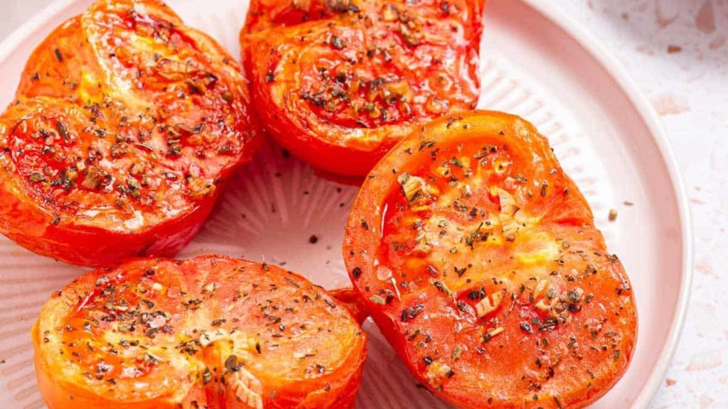 Four sliced and air-fried tomatoes on a plate with spices.
