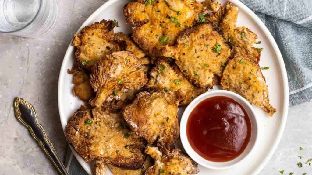 Air fryer oyster mushrooms on a plate served with tomato sauce will glasses of water and fork beside.