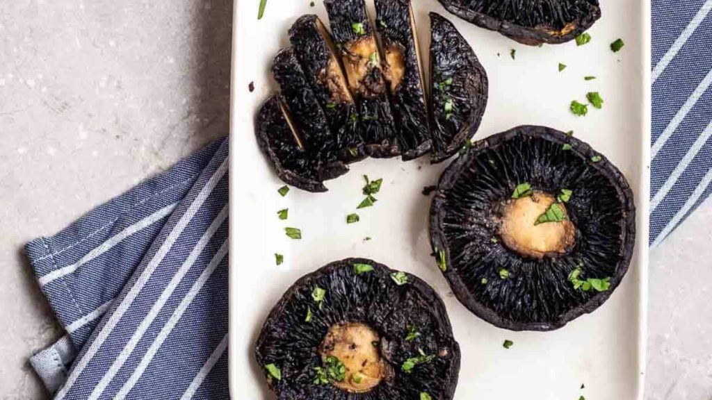 4 portobello mushrooms on a plate topped with chopped cilantro on a blue striped teacloth.