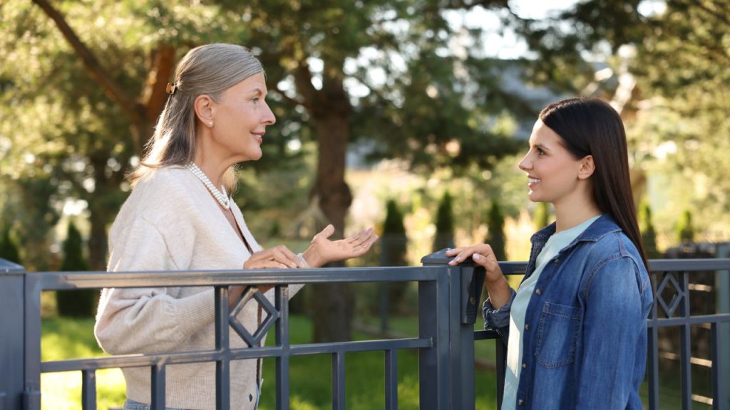 neighbor of women speaking to eachother over a fence