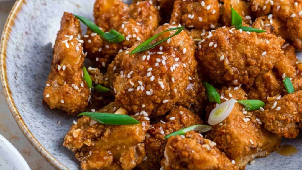 A blue bowl filled with cauliflower wings topped with sesame seeds and green onion.