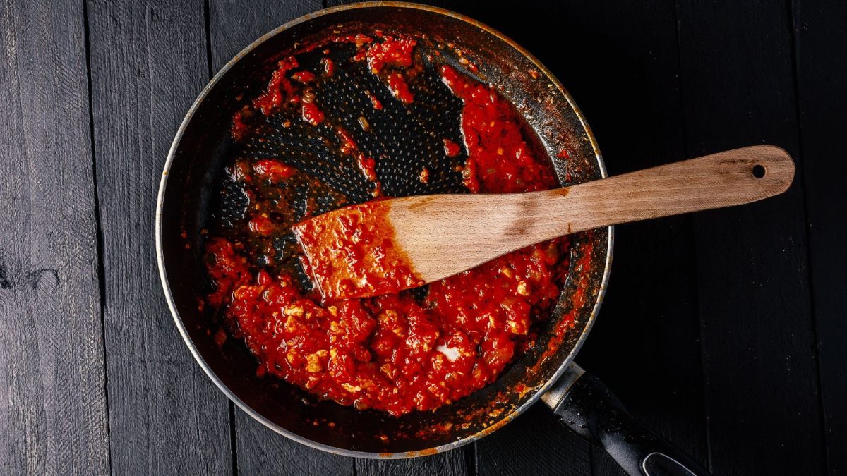Classic homemade tomato sauce in the pan on a wooden chopping board on brown background, top view. Pasta, pizza tomato sauce. Vegetarian food