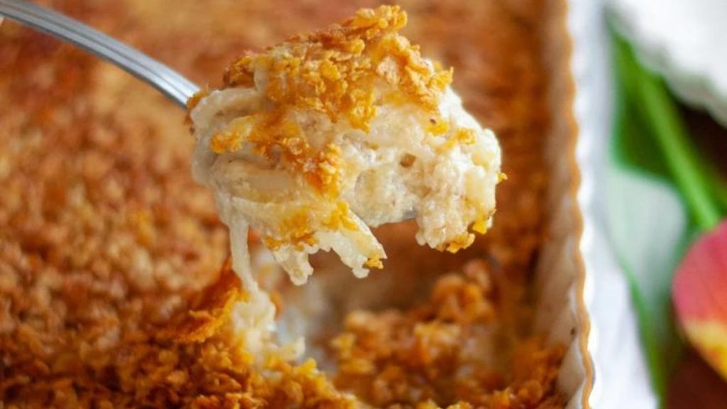 24 Potato Recipes You’ll Never Get Tired Of 15 Close up for a spoon with a big scoop of cheesy potato casserole with corn flakes. The spoon has just been scooped out of the 9x13 dish and is ready to serve.