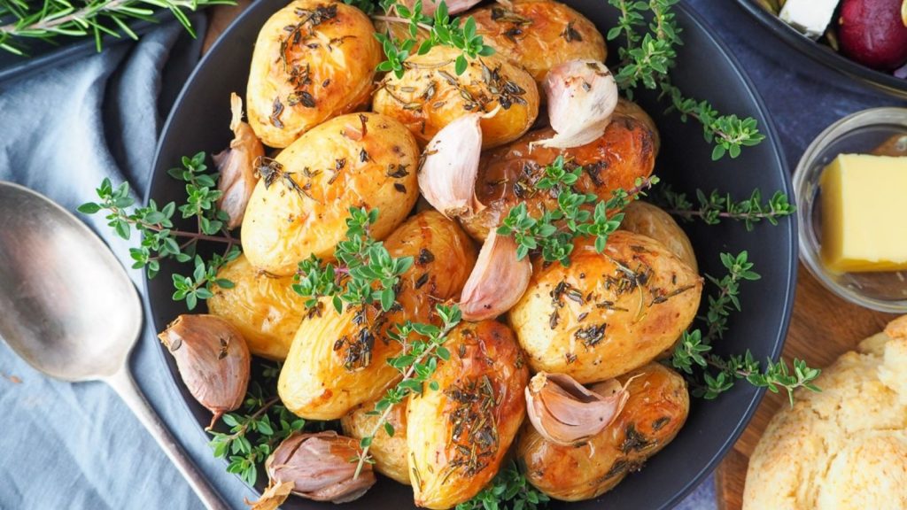 24 Potato Recipes You’ll Never Get Tired Of 16 Roasted mini potatoes in a serving dish garnished with fresh herbs, silver serving spoon to the side, fresh damper, pat of butter, beetroot salad and slow cooker roast lamb on the side.